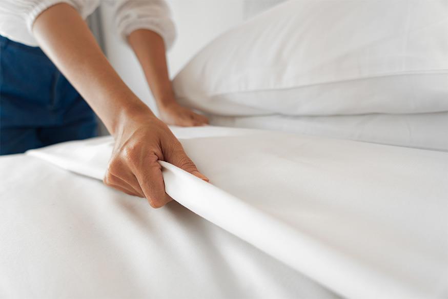 woman straightening sheets on a comfortable looking hotel bed